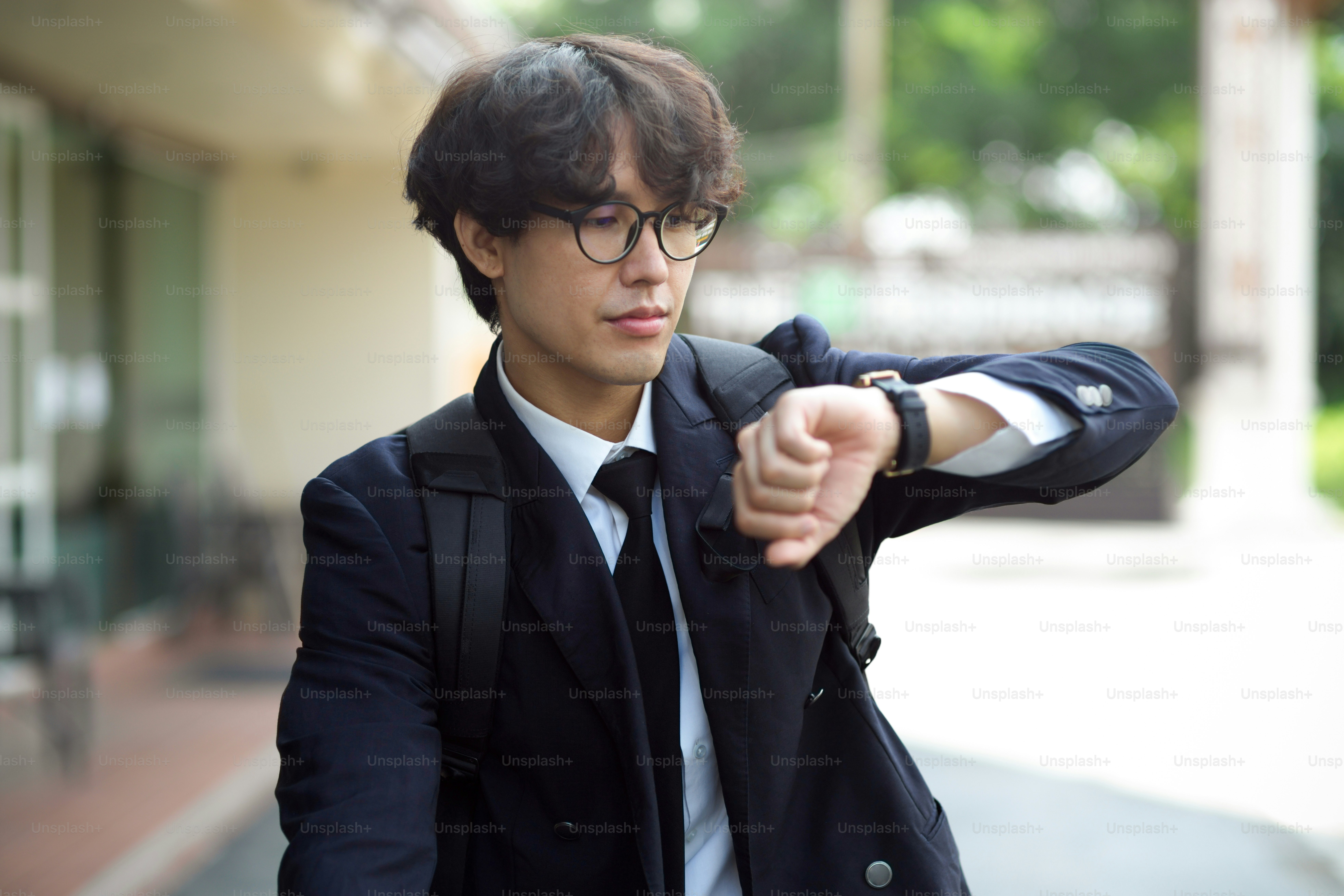Handsome young businessman checks the time on his wristwatch while walking down the street.