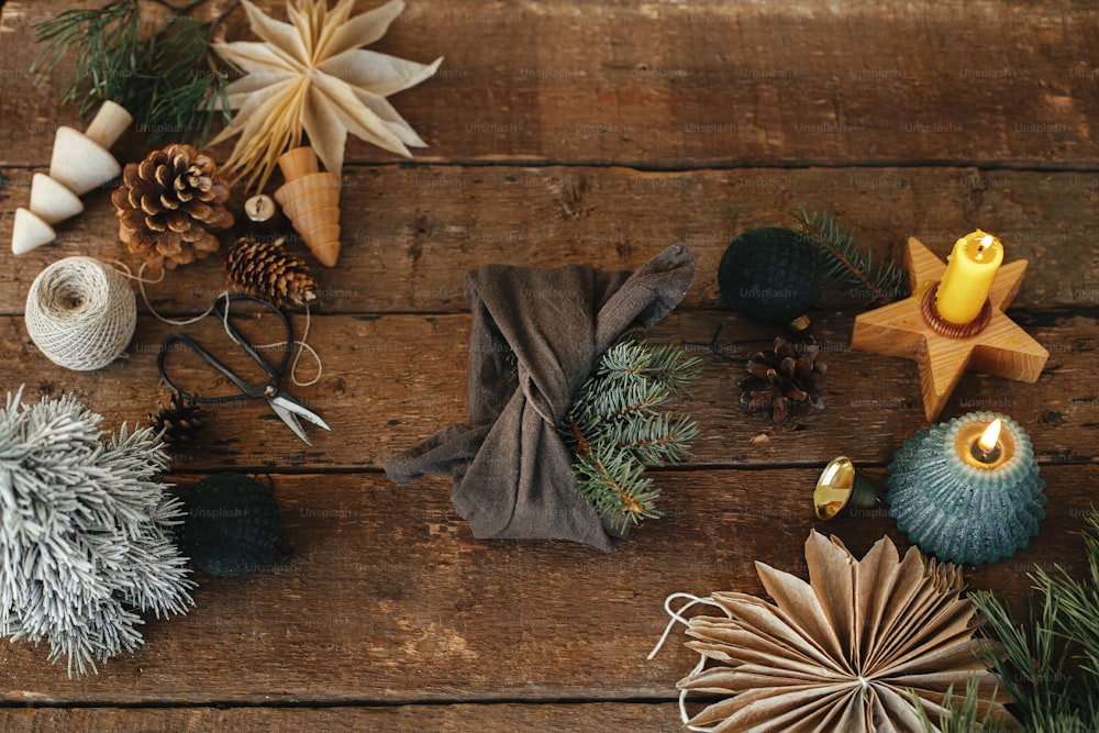休日の装飾が施された素朴な木製のテーブルの上にモミの枝で布に包まれたスタイリッシュなクリスマスプレゼント。ゼロウェイストの冬休みとギフトフラットレイ。風呂敷エコプレゼント