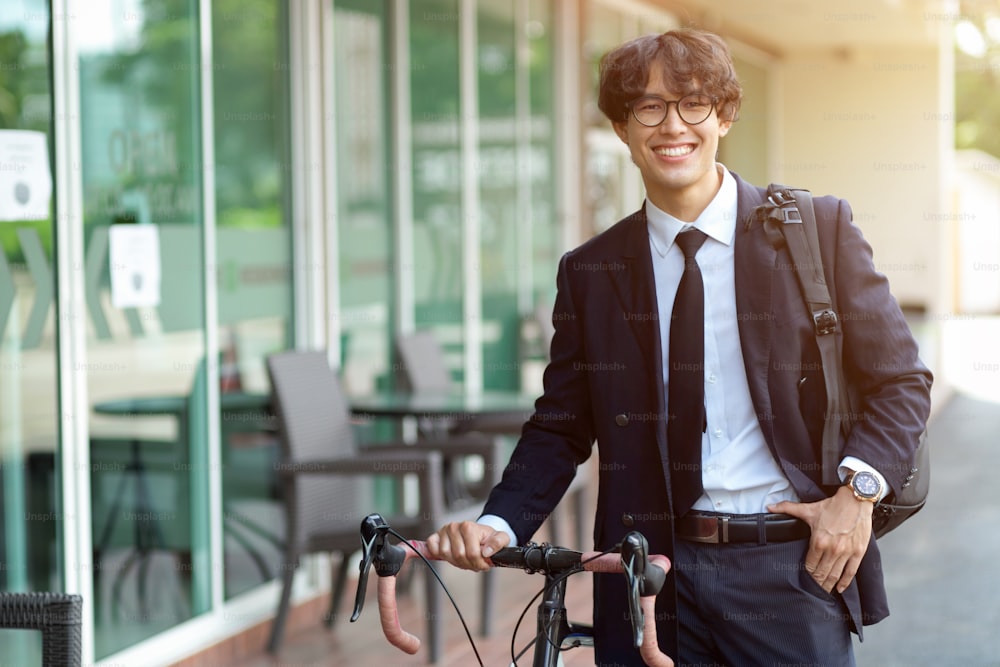 Confident handsome asian young businessman going to work by bike, walking outdoors with a bicycle in a modern street.