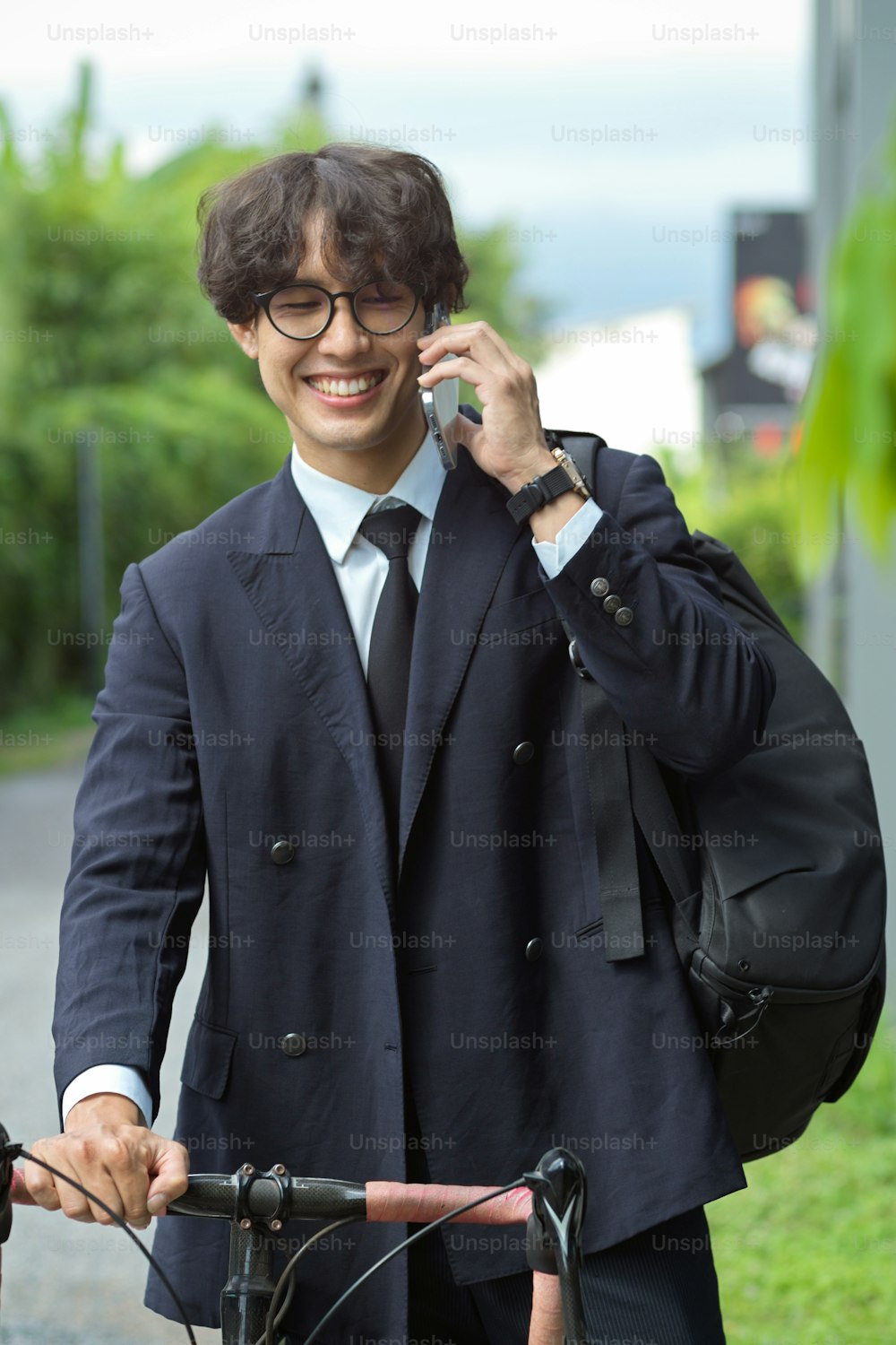 Urban successful businessman talking on the phone while walking and pushing bicycle to work on the street.