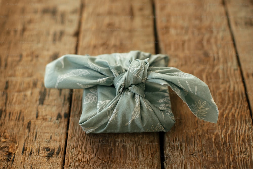 Furoshiki regalo ecologico. Elegante regalo avvolto in tessuto su tavolo rustico in legno. Buone Feste. Vacanze invernali, compleanni o festa della mamma a rifiuti zero
