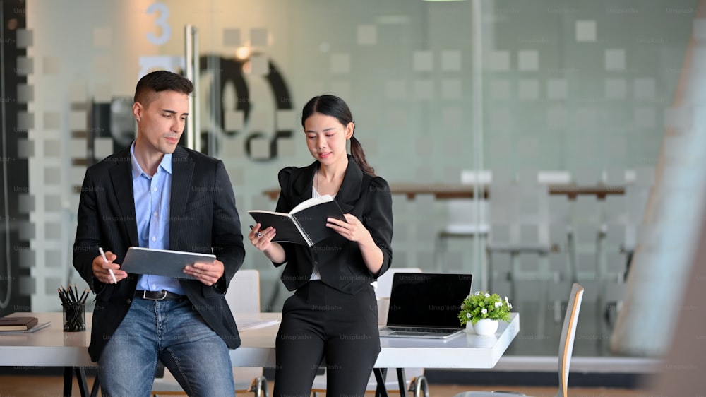 Successful businessman and elegant female manager standing in modern office and having a business talk