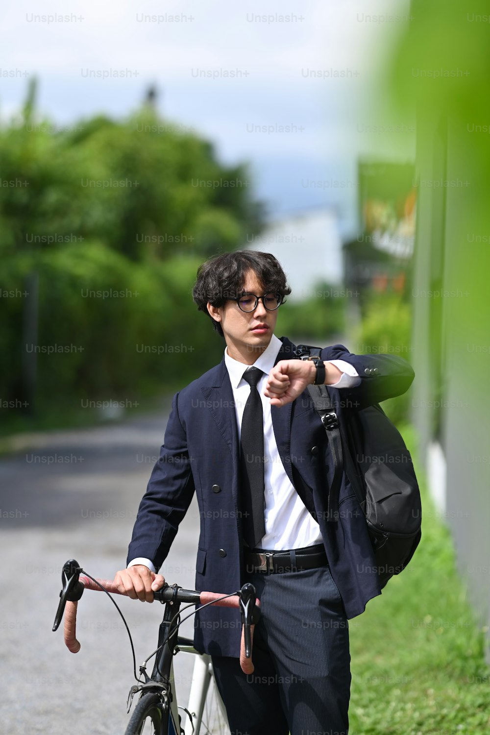 Empresário asiático verificando o tempo em seu relógio de pulso e se deslocando para o trabalho com bicicleta.