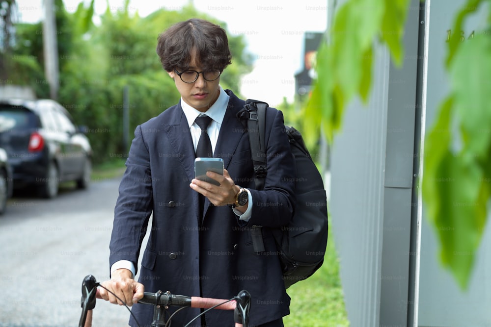 Young asian businessman looking at messages on mobile phone while riding bicycle in the city.