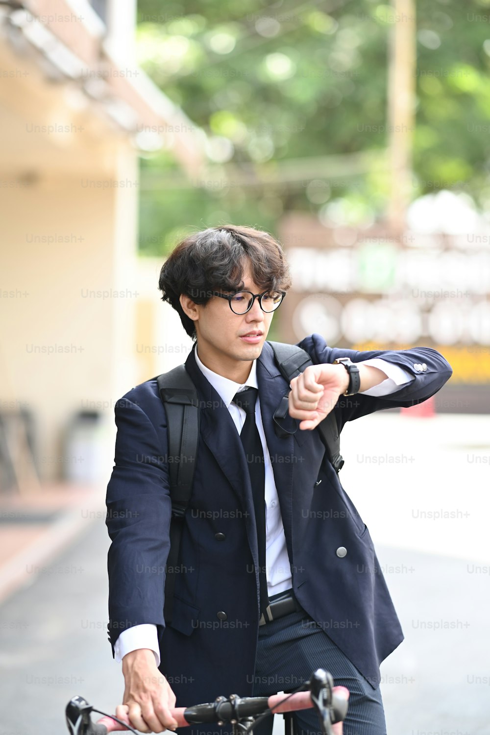 Young businessman commuting to work with a bicycle and checking time on wrist watch.