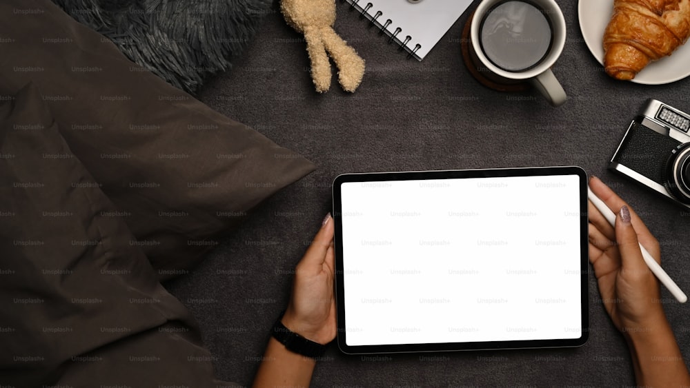 Manos de mujer sosteniendo una tableta digital de maqueta con pantalla en blanco.