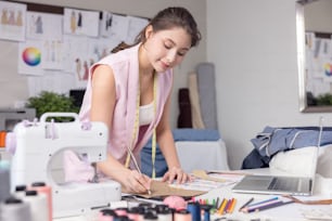 Ritratto di una donna giovane e attraente sul tavolo di uno stilista alla moda, circondata da campioni tessili a colori. Donna attraente che lavora in uno studio di moda con manichini e tessuti colorati.
