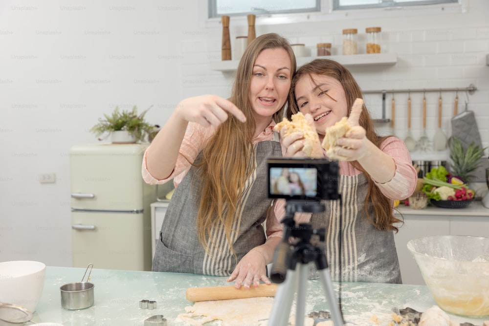 Con una cámara digital en vivo en la cocina, madre e hija sonríen y se divierten mientras preparan juntas la masa de galletas, la hija aprende a hacer galletas con su madre.