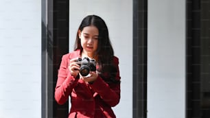 Pretty young asian woman photographer checking picture on her camera while standing near window.