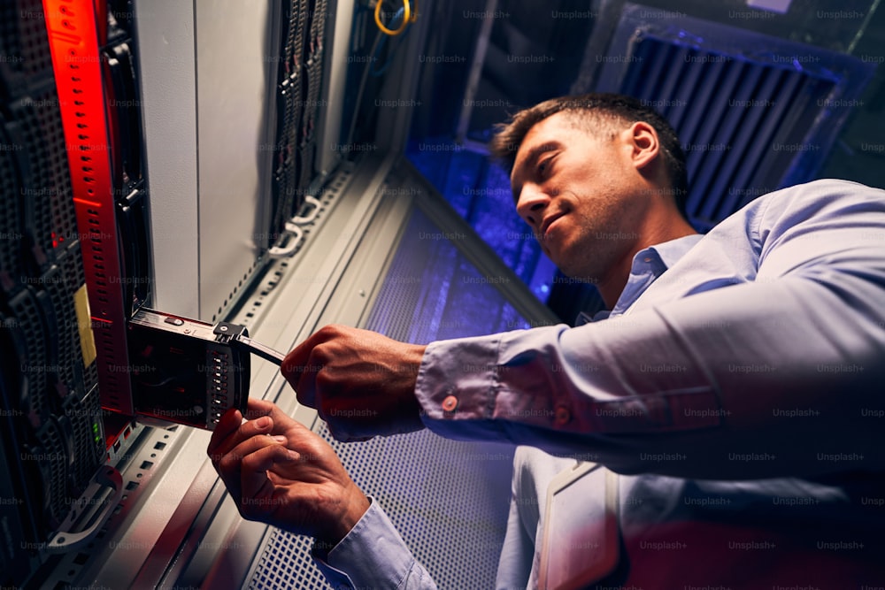 Low angle of focused skilled IT technician inserting hard disk drive into network computer