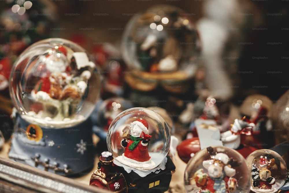 Stylish christmas snow globes in window shop. Christmas festive street decor in european city street for winter holidays. Magic little xmas scene, holiday winter fair. Merry Christmas!