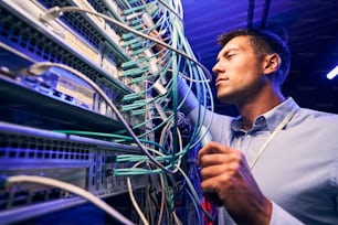 Focused serious experienced data center IT technician doing performance checking of twisted-pair cables