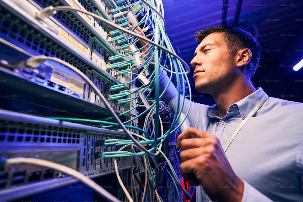 Focused serious experienced data center IT technician doing performance checking of twisted-pair cables