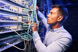Serious concentrated data center IT technician checking network cables connected to server
