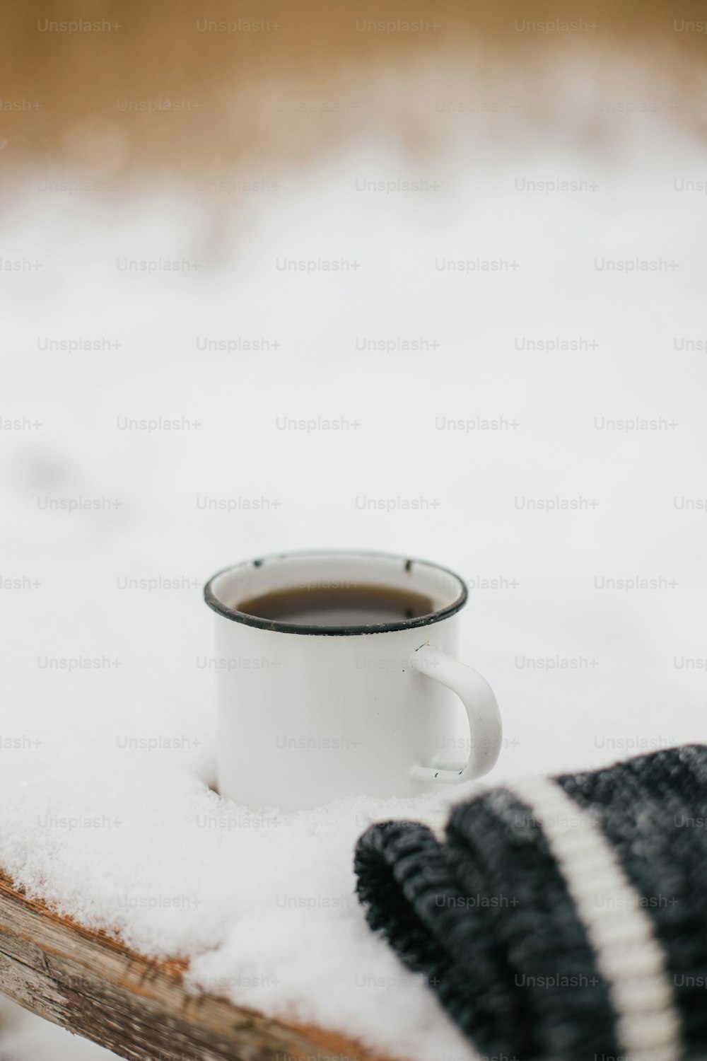 Warm cup of tea and cozy knitted gloves in snow on wooden bench in winter park. Hiking and traveling in cold season. Wanderlust. Space for text. Winter time