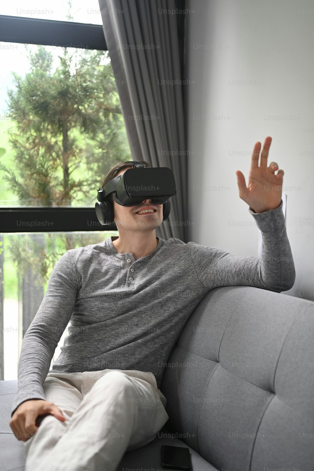 Hombre con gafas de realidad virtual jugando videojuegos mientras está sentado en el sofá.