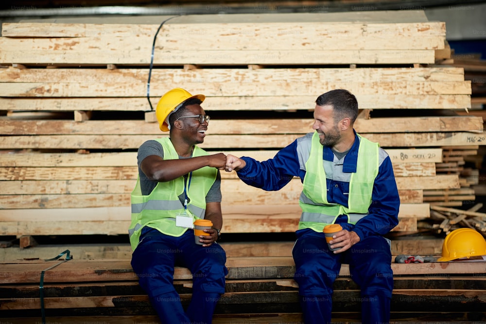 Happy workers having fun and fist bumping during their coffee break at lumber warehouse.