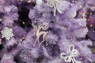 Elegante juguete de reno con purpurina en el árbol de Navidad púrpura moderno con adornos y luces en el frente de la tienda o en la fachada del edificio. Decoración callejera festiva navideña para las vacaciones de invierno. Feliz Navidad