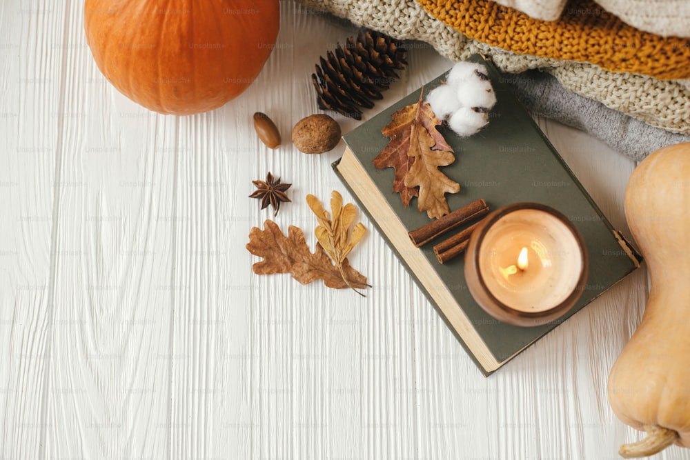 가을 플랫은 복사 공간이 있습니다. 호박, 아늑한 스웨터, 단풍, 불타는 촛불, 방에 있는 흰색 나무 배경에 빈티지 책. 안녕하세요 가을, 아늑한 느린 생활.  행복한 추수 감사절