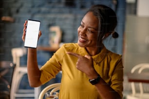 Beautiful young african american woman showing a smartphone while sitting in a cafe