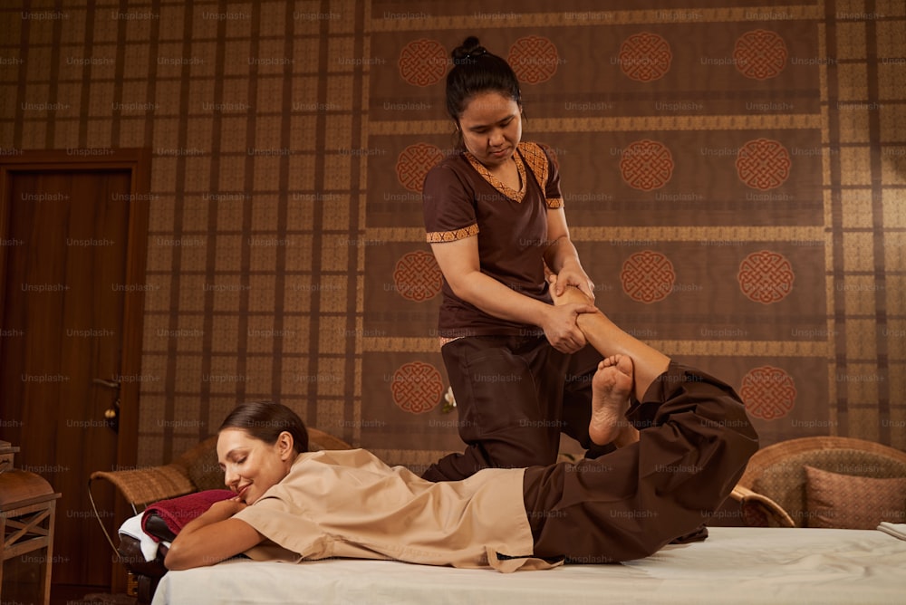 Serious concentrated masseuse using reverse half lotus with leg lift technique during Thai massage session