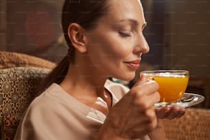 Portrait of tranquil pleased female spa client inhaling aroma of sea buckthorn tea