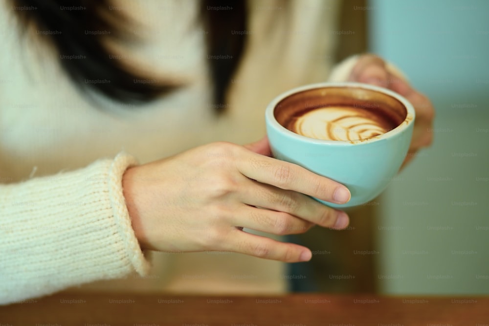 Vista de perto a jovem mulher em suéter branco segurando xícara de café quente.