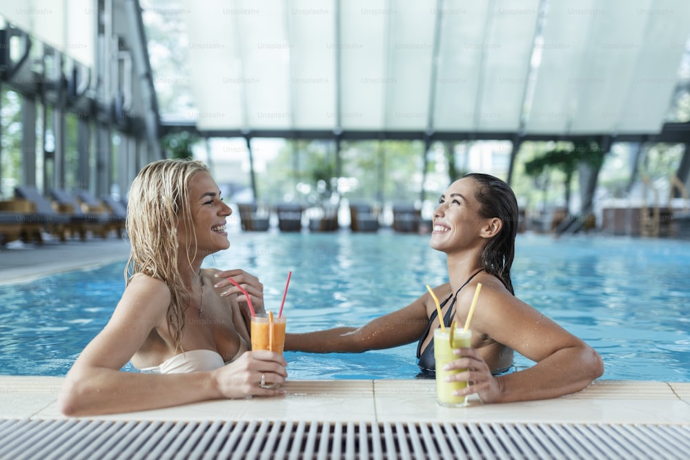 Women friends drink, cocktail mojito on pool bar, wear bikini luxury hotel near beach on tropical island relax. Beautiful young women having fun in swimming pool, drinking cocktail, smiling.