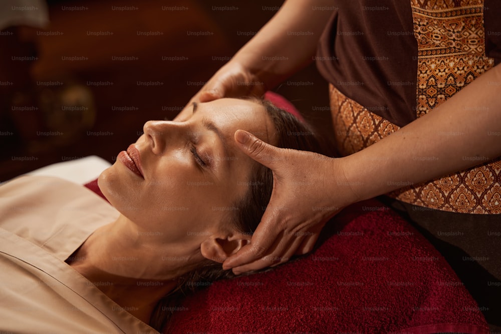 Massaggiatore professionista che preme i punti di agopuntura del palmo della mano sulla fronte della paziente femminile