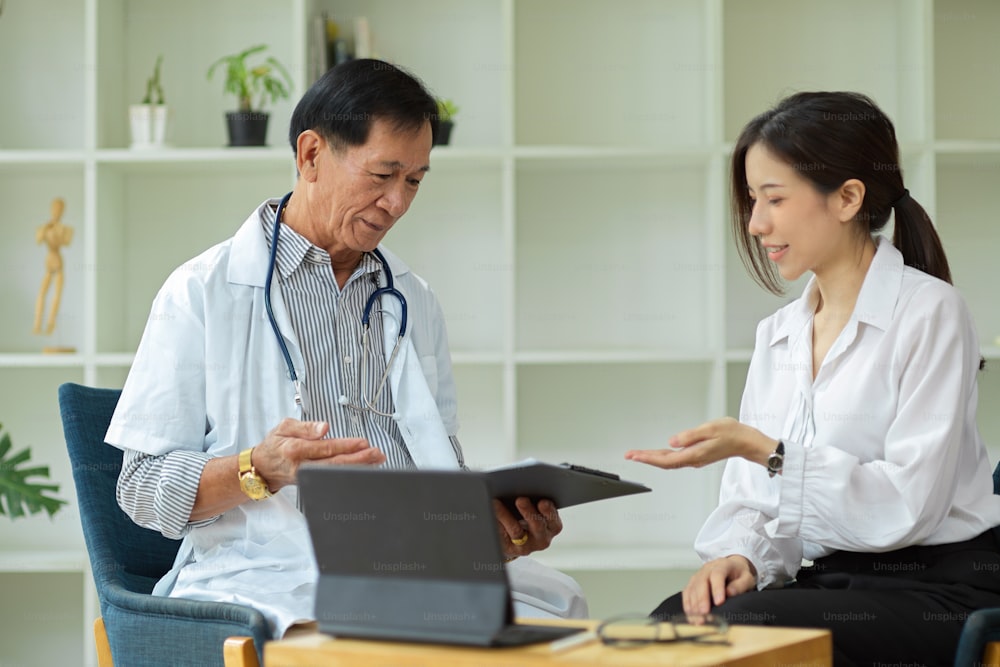 Eine asiatische Patientin berät sich im Gesundheitszentrum mit einem Facharzt mittleren Alters über ihre Verletzungspläne.