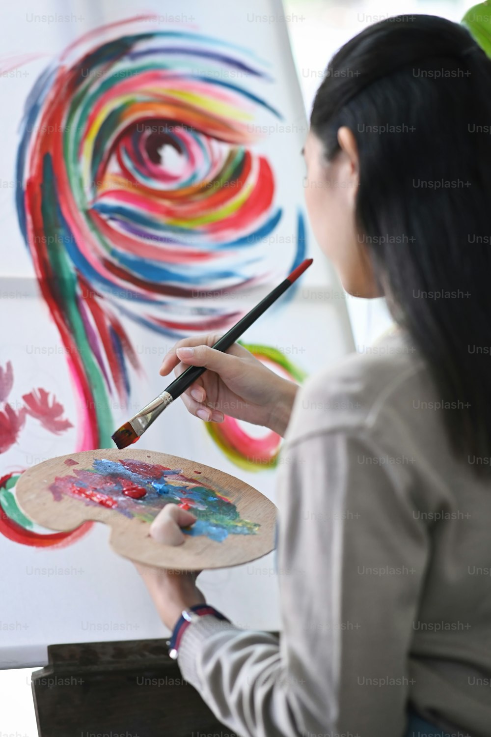 Vista trasera de una artista femenina pintando con acuarela sobre lienzo.