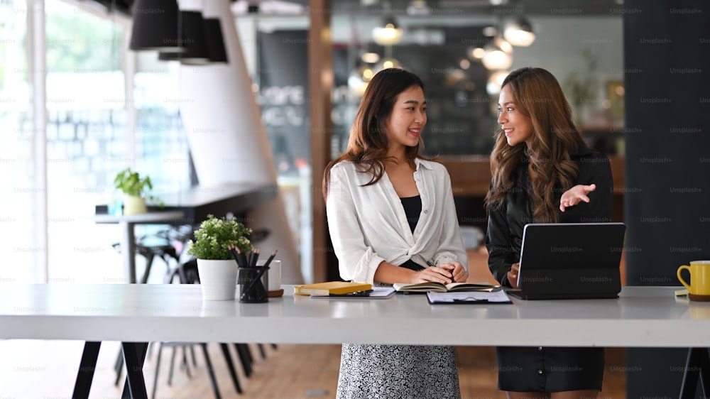 Two cheerful businesswoman working on new project together in modern workplace.