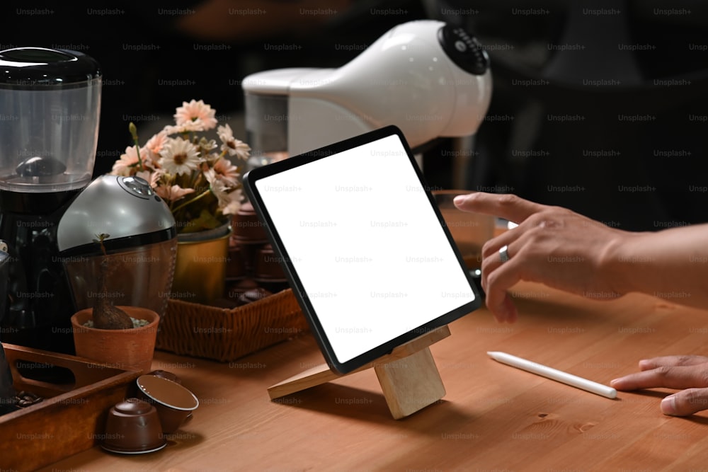 Gros plan sur un homme barista utilisant une tablette numérique près d’une machine à café.