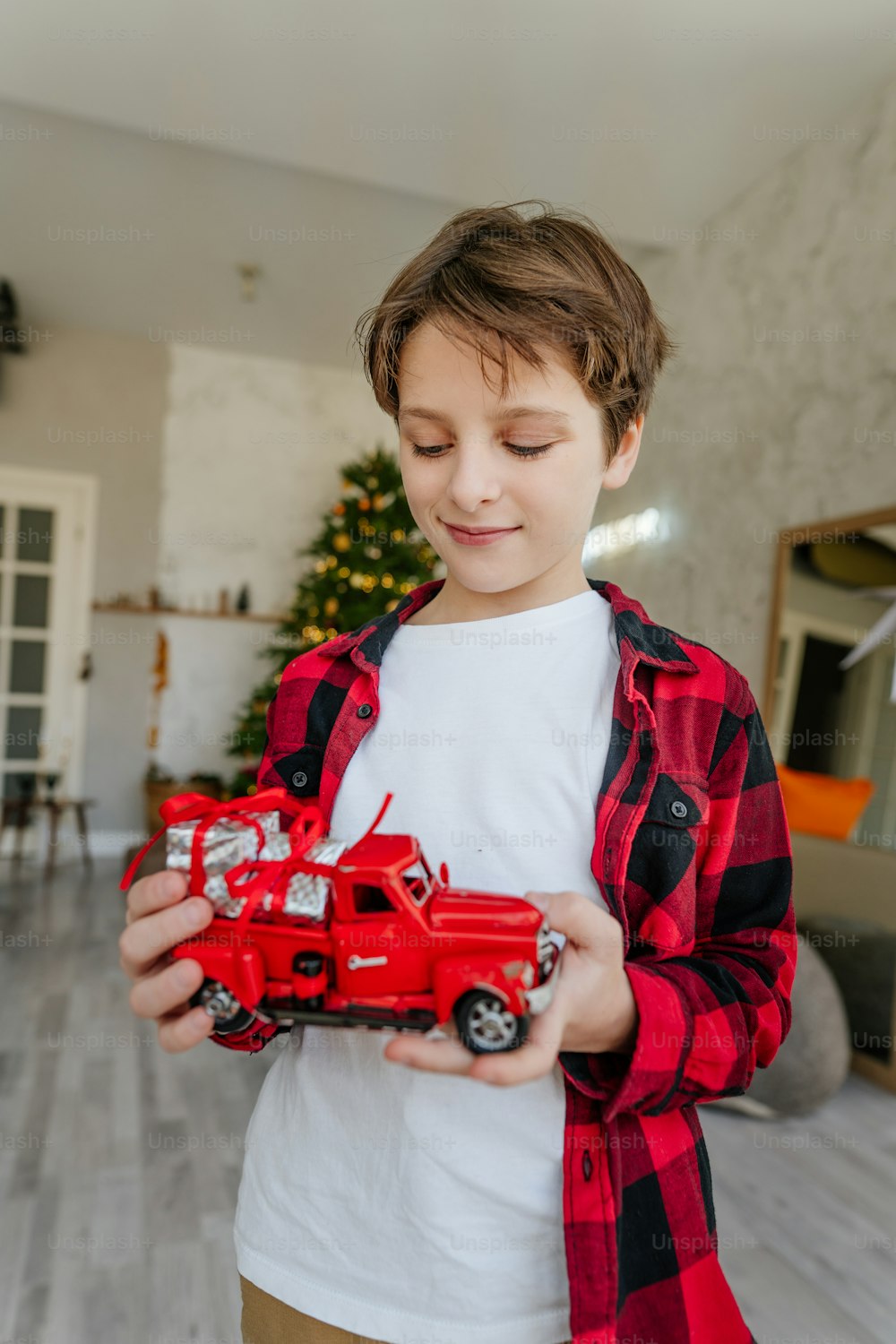 Niño jugando con coche de juguete rojo y cajas de regalo de Navidad.