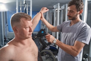 Il fisioterapista tratta i muscoli del torace dell'uomo con un dispositivo a percussione massaggiante. Trattamento fisioterapico