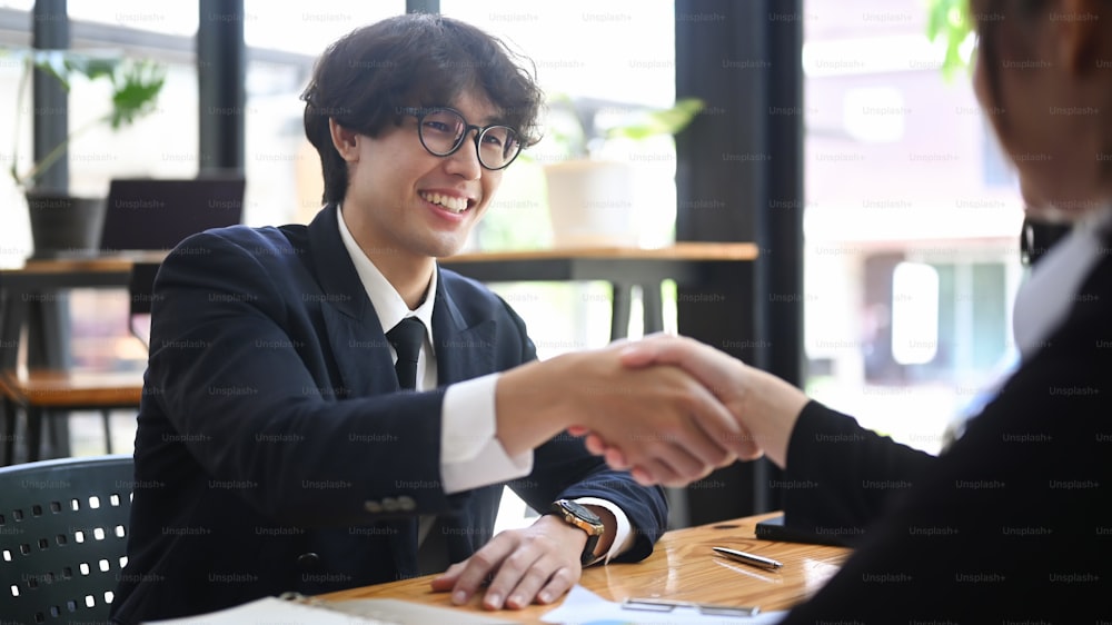 Smiling businessman in formal wear shaking hands with his business partner after negotiations.