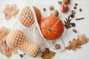 Pumpkins in string bag, apples, nuts and autumn leaves on white wooden background. Autumnal Flat lay. Zero waste concept, plastic free shopping. Harvest. Happy Thanksgiving