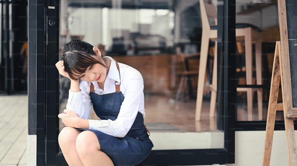 Empresaria de pequeña empresa estresada sentada frente a su cafetería.