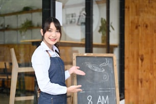 Jeune femme entrepreneure debout devant un tableau noir à la porte de son café.