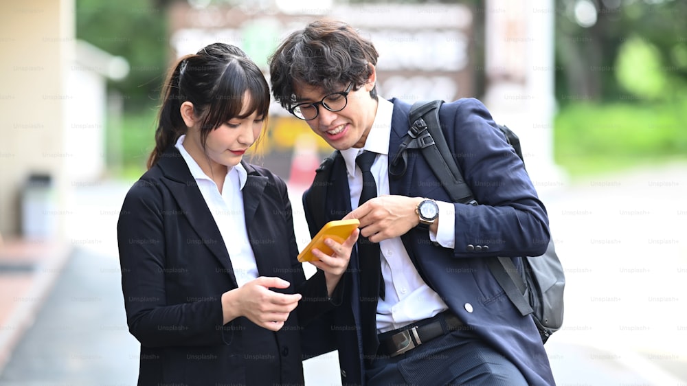 Two business colleagues using smart phone while standing outdoors at the city streets.