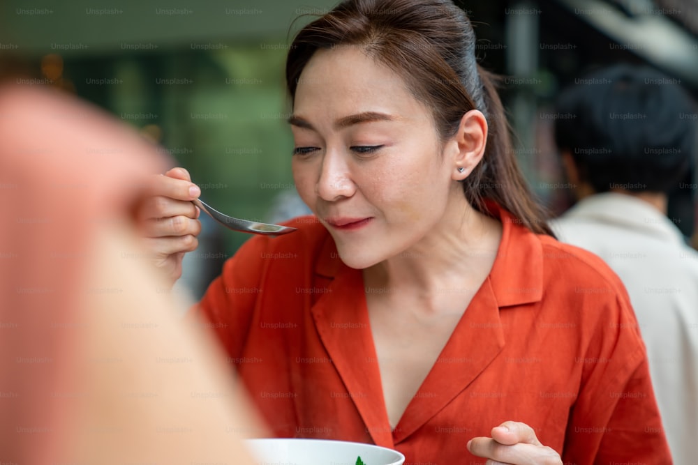 タイ・バンコク市のチャイナタウン・ストリート・ナイトマーケットで一緒に夕食をとるアジア人の友人の観光客のグループ。男性と女性の友人は、アウトドアライフスタイルのナイトライフと屋台の食べ物を食べることを楽しんでいます