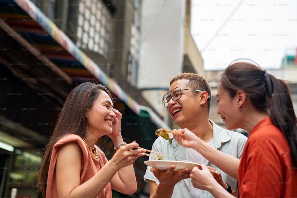 Gruppo di donne asiatiche e persone LGBTQ amici turisti si divertono a mangiare insieme i tradizionali gyoza di gamberetti fritti di street food al mercato notturno di Chinatown a Bangkok, in Thailandia. Concetto di viaggio e street food
