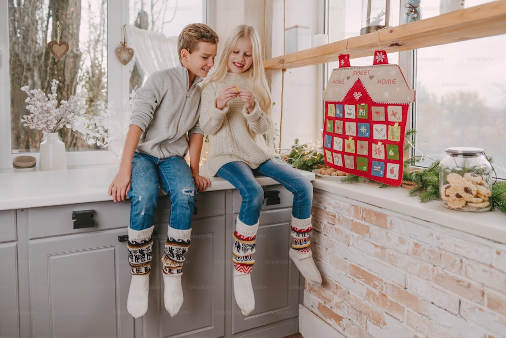 Children reading tasks from Christmas handmade advent calendar in a house shape to countdown the days until Christmas on the wall in the room.