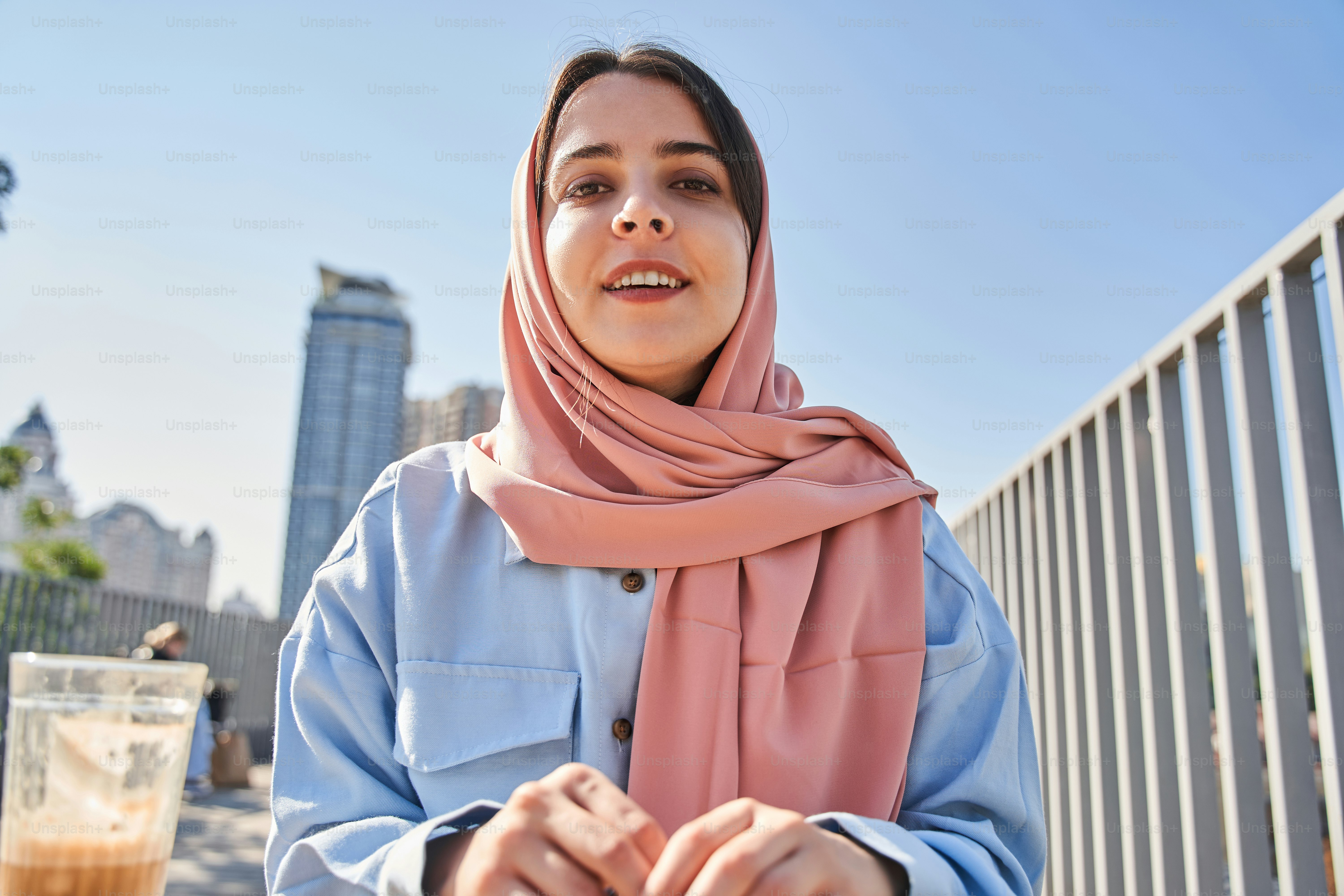 Low angle view of the multiracial blogger woman wearing head scarf broadcasting at the street with high towers at the background