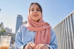 Low angle view of the multiracial blogger woman wearing head scarf broadcasting at the street with high towers at the background