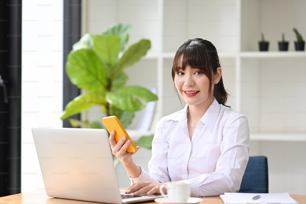 Attractive businesswoman holding smart phone and working with computer laptop.