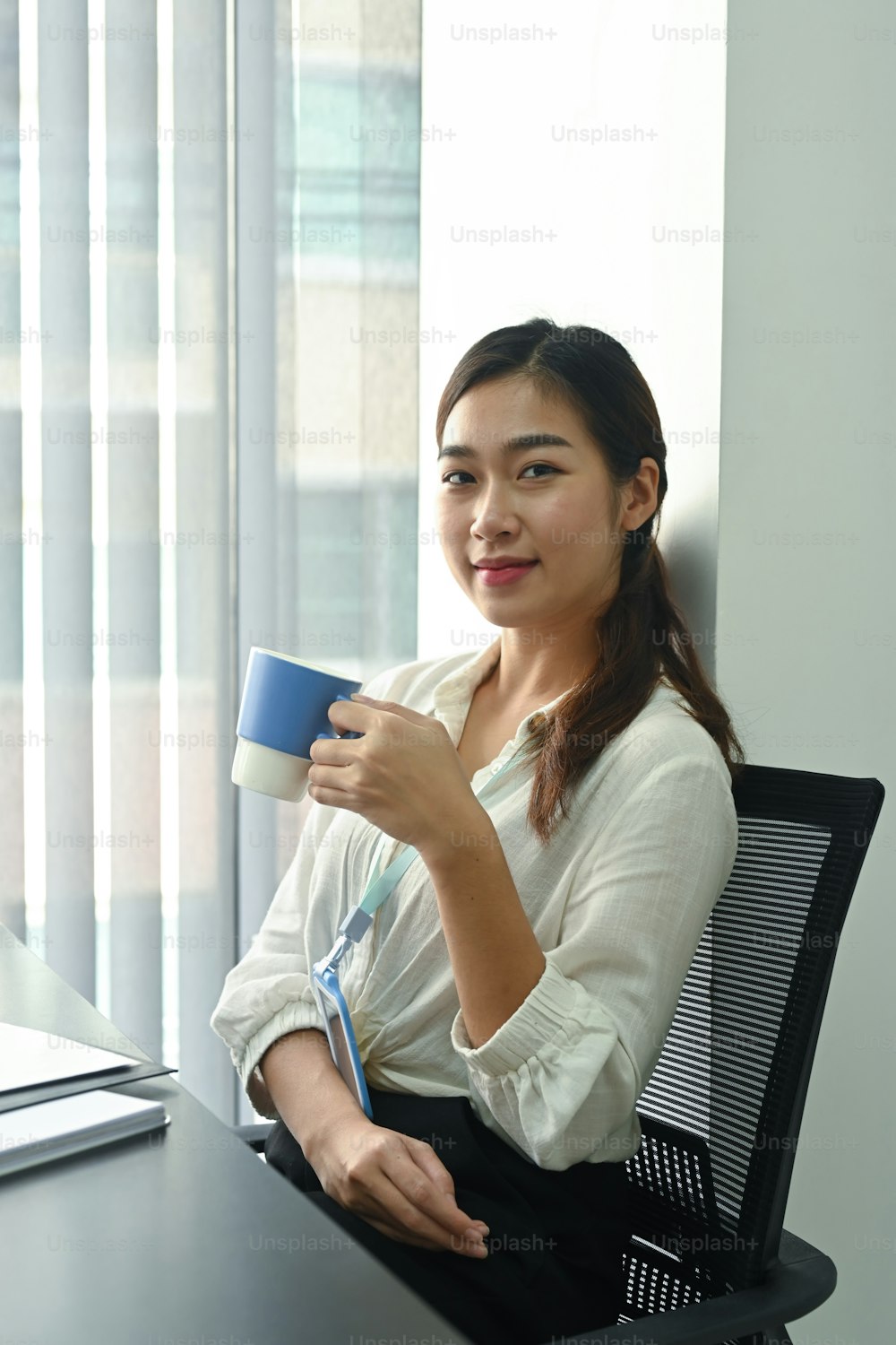 Portrait of female office worker holding coffee cup and smiling to camera.