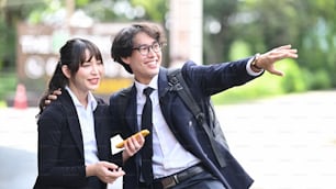 Two cheerful young business people talking to each other while standing outdoors at the city streets.