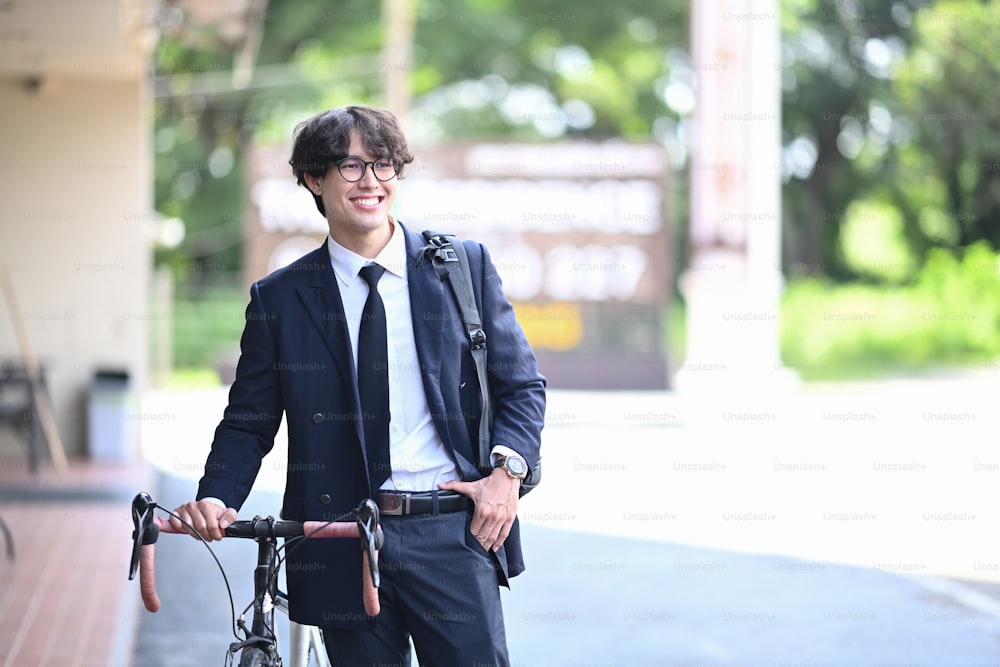 웃고 있는 젊은 사업가가 거리에서 자전거를 타고 걷고 있다. 에코 교통 개념입니다.