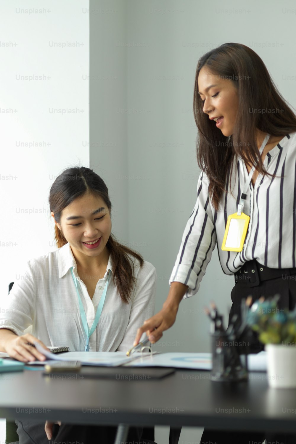 Female asian mentor teaching female trainee intern looking at report papers, female colleagues working together in office.